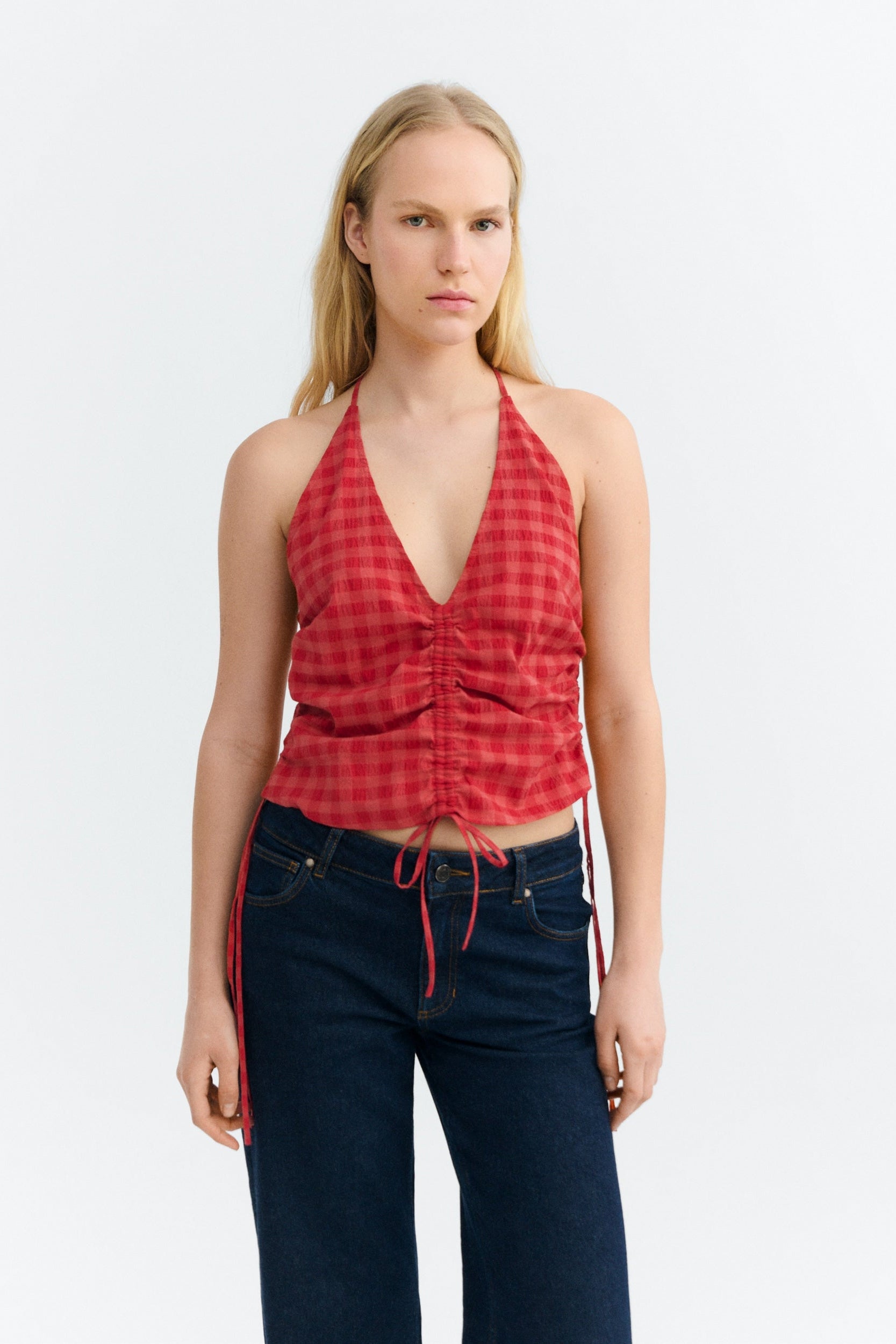 Woman wearing a red plaid halter top and dark blue jeans on a white background
