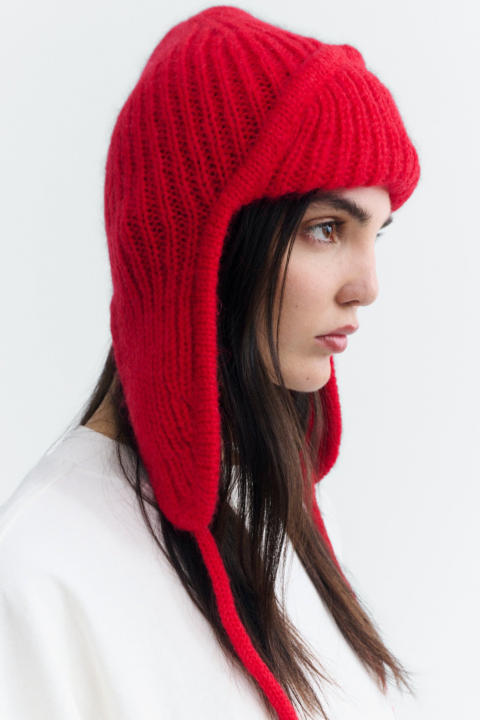 A woman wearing a bright red knit ear-flap beanie hat, shown in profile against a clean white background.