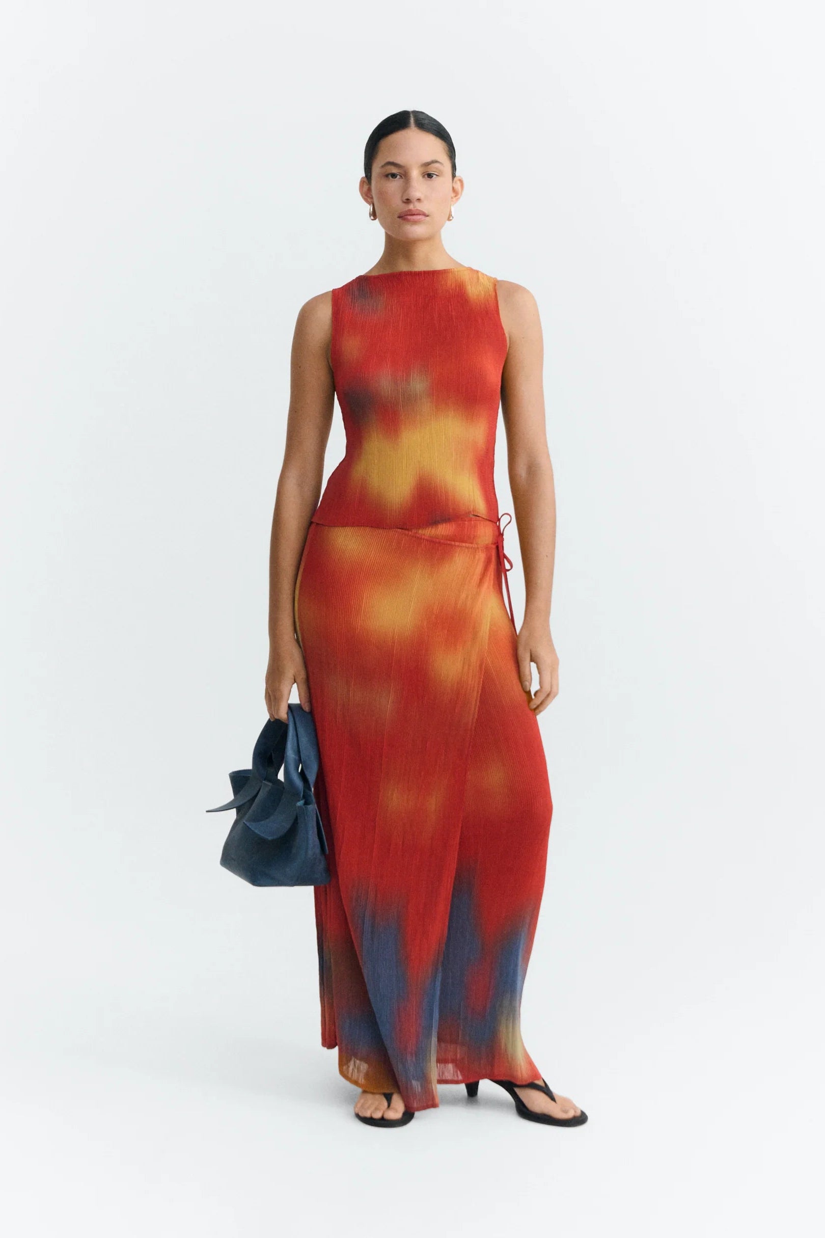 Woman wearing a tie-dye dress with a blue handbag on a white background