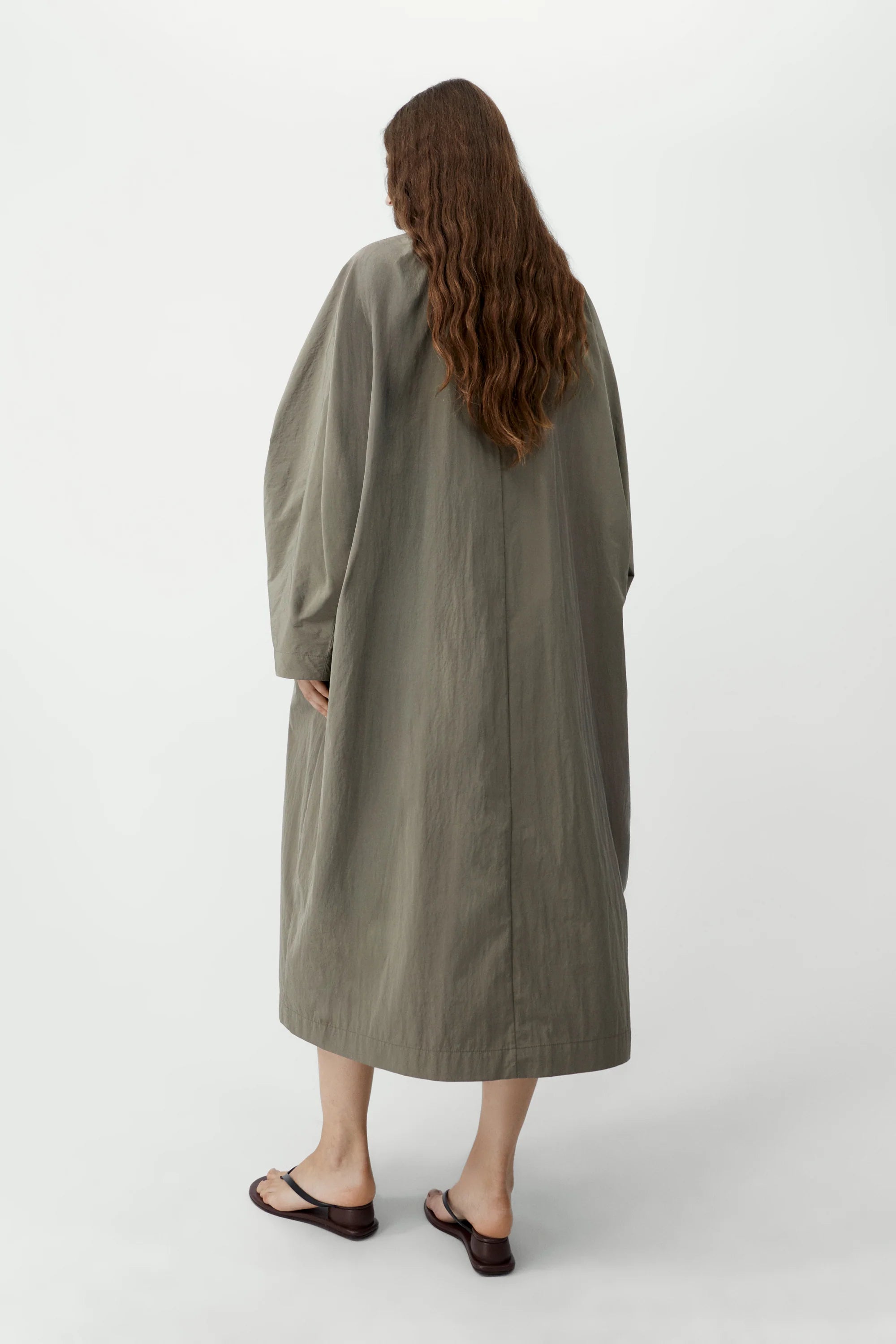 Person wearing a long olive green coat on a white background