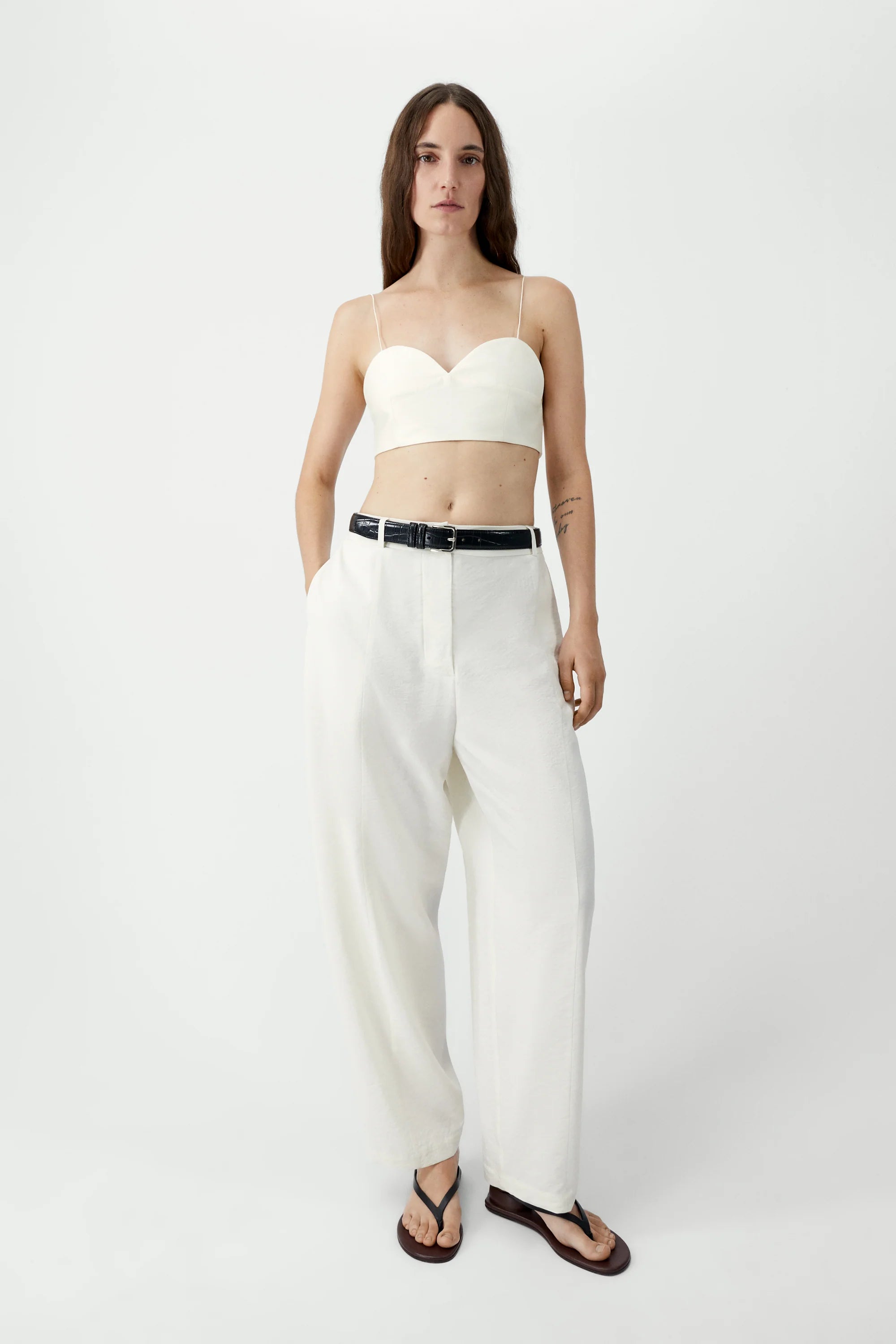 Woman wearing a white bralette top and pants on a white background