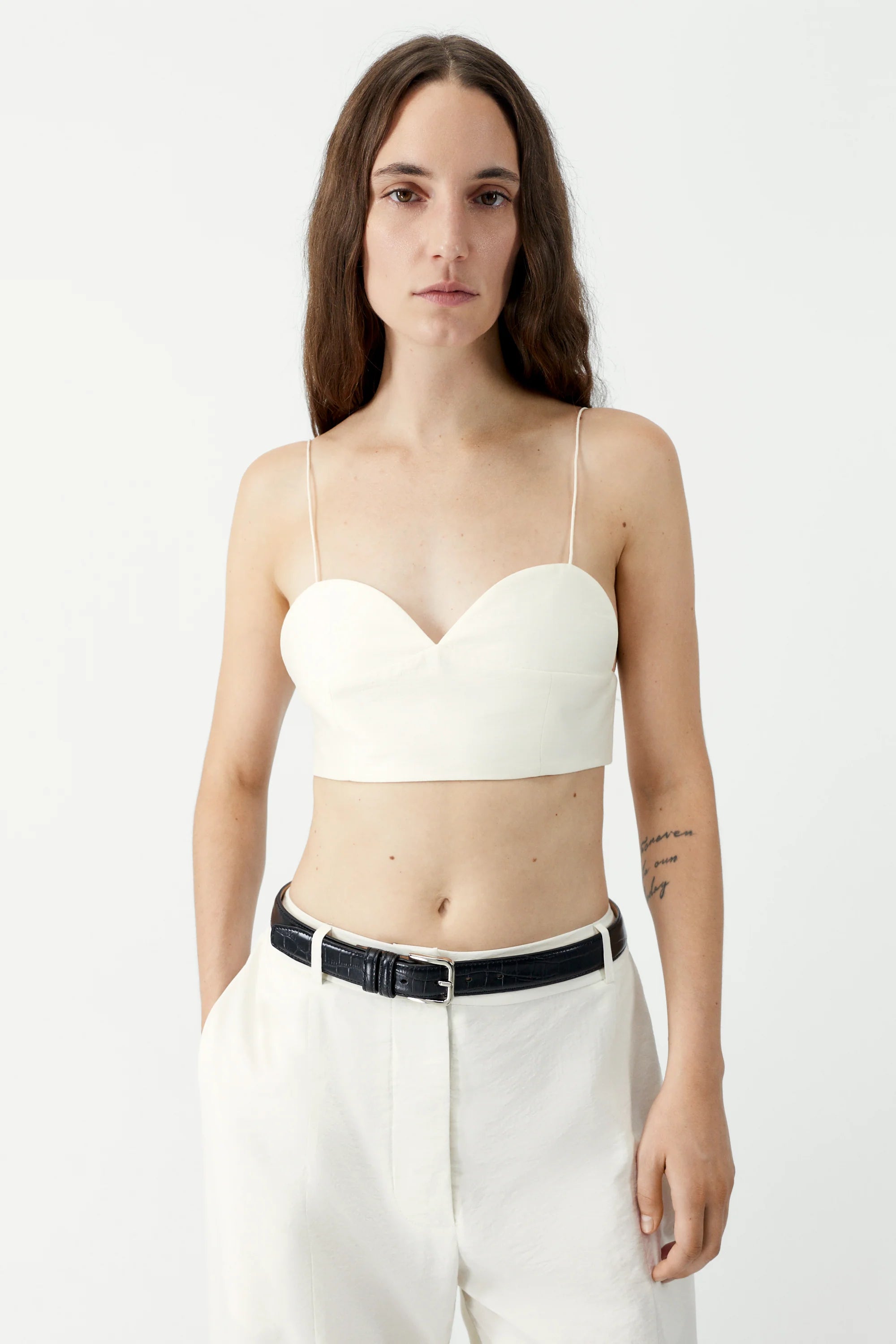 Woman wearing a white bralette top and white pants on a plain background