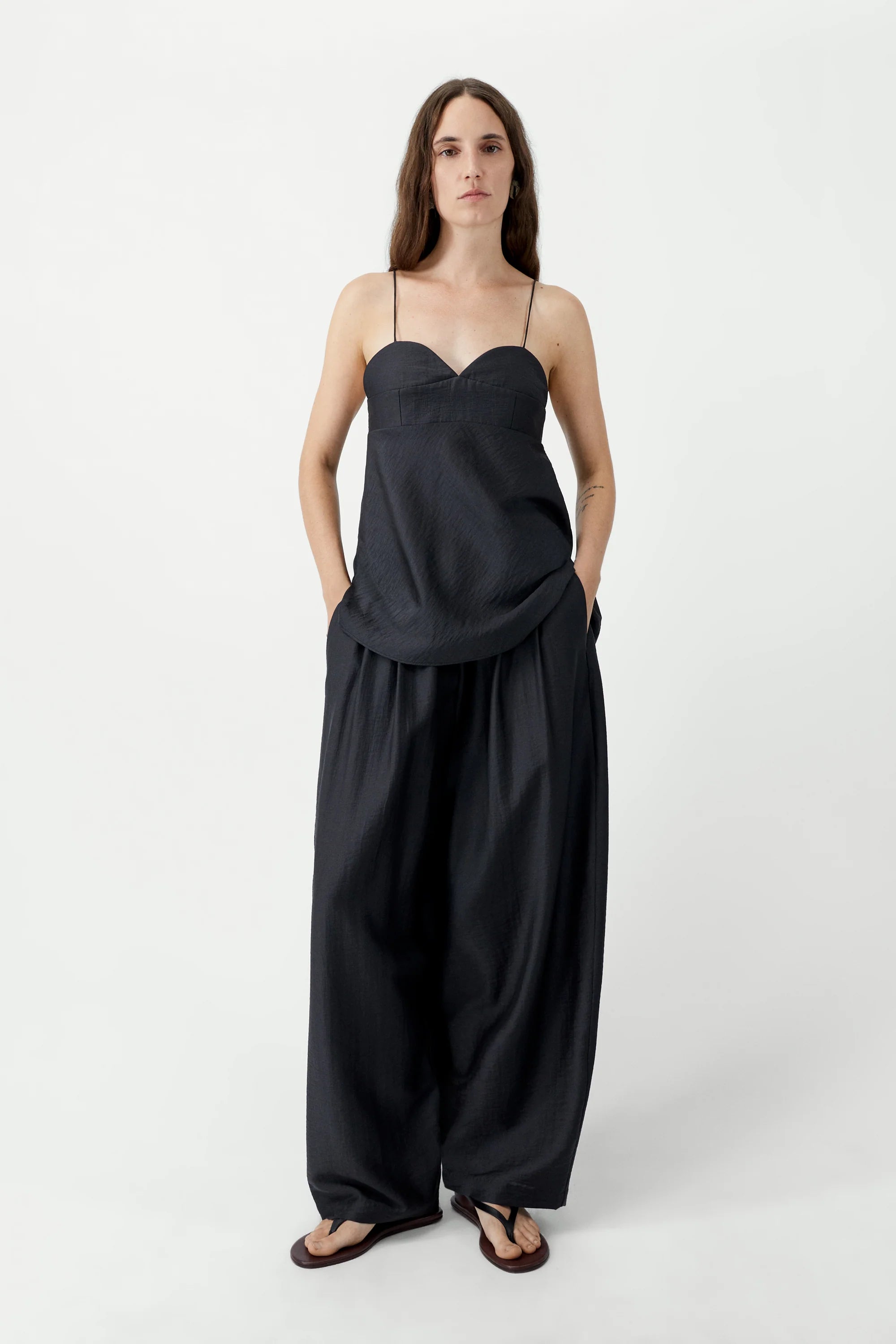 Woman wearing a black slip dress with wide-leg pants on a white background