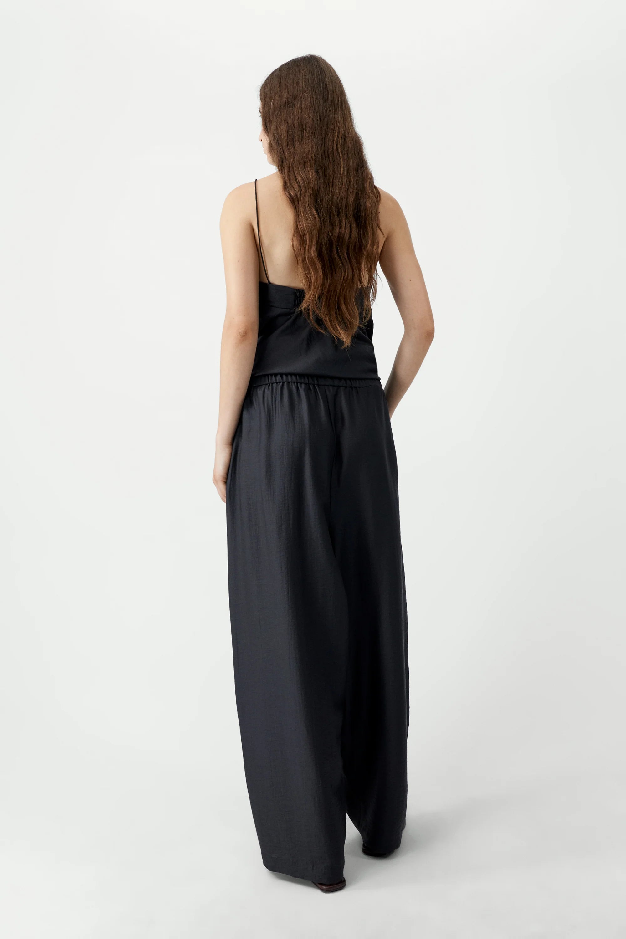 Person wearing a black sleeveless top and wide-leg pants on a white background