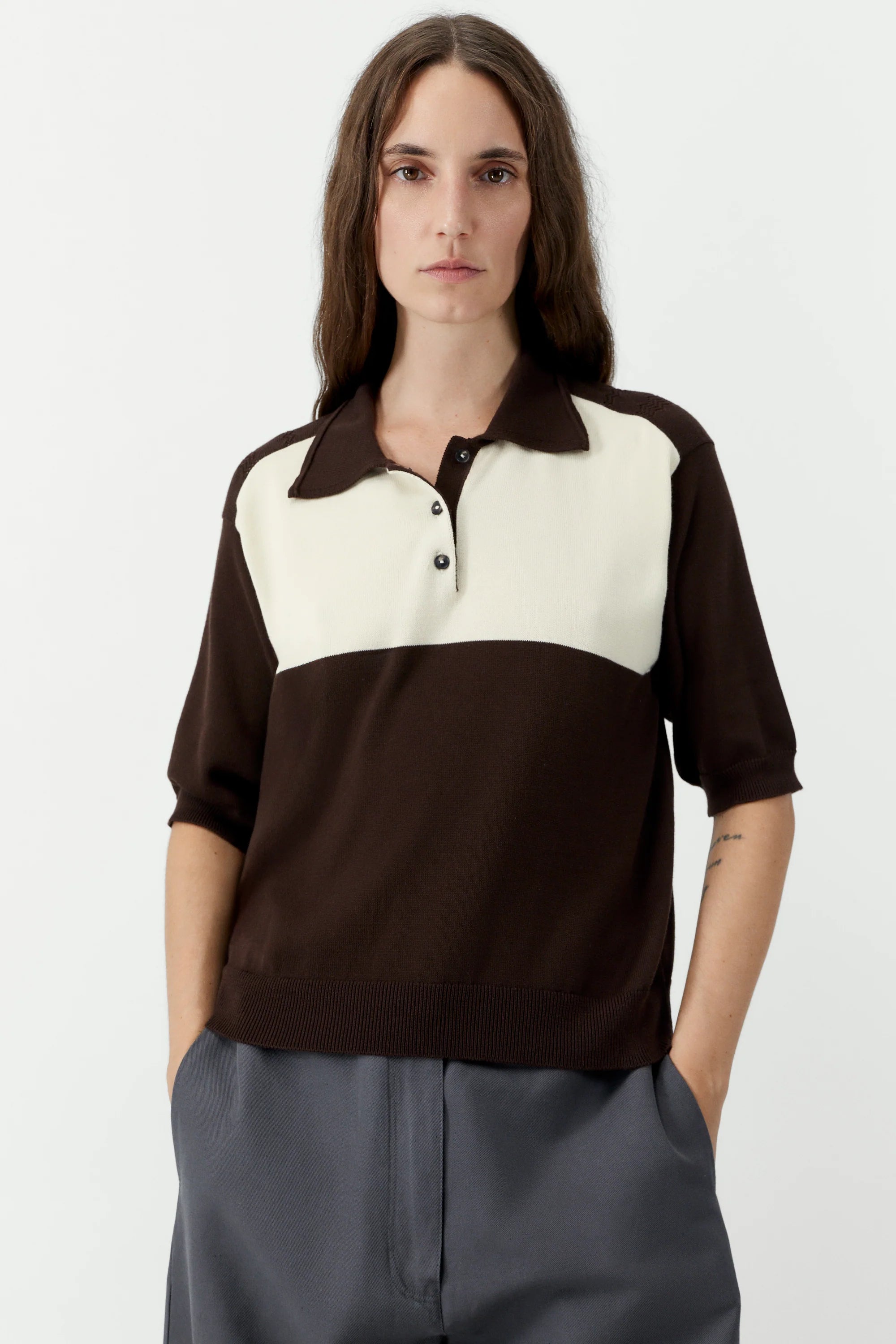 Woman wearing a two-tone brown and white polo shirt on a plain background