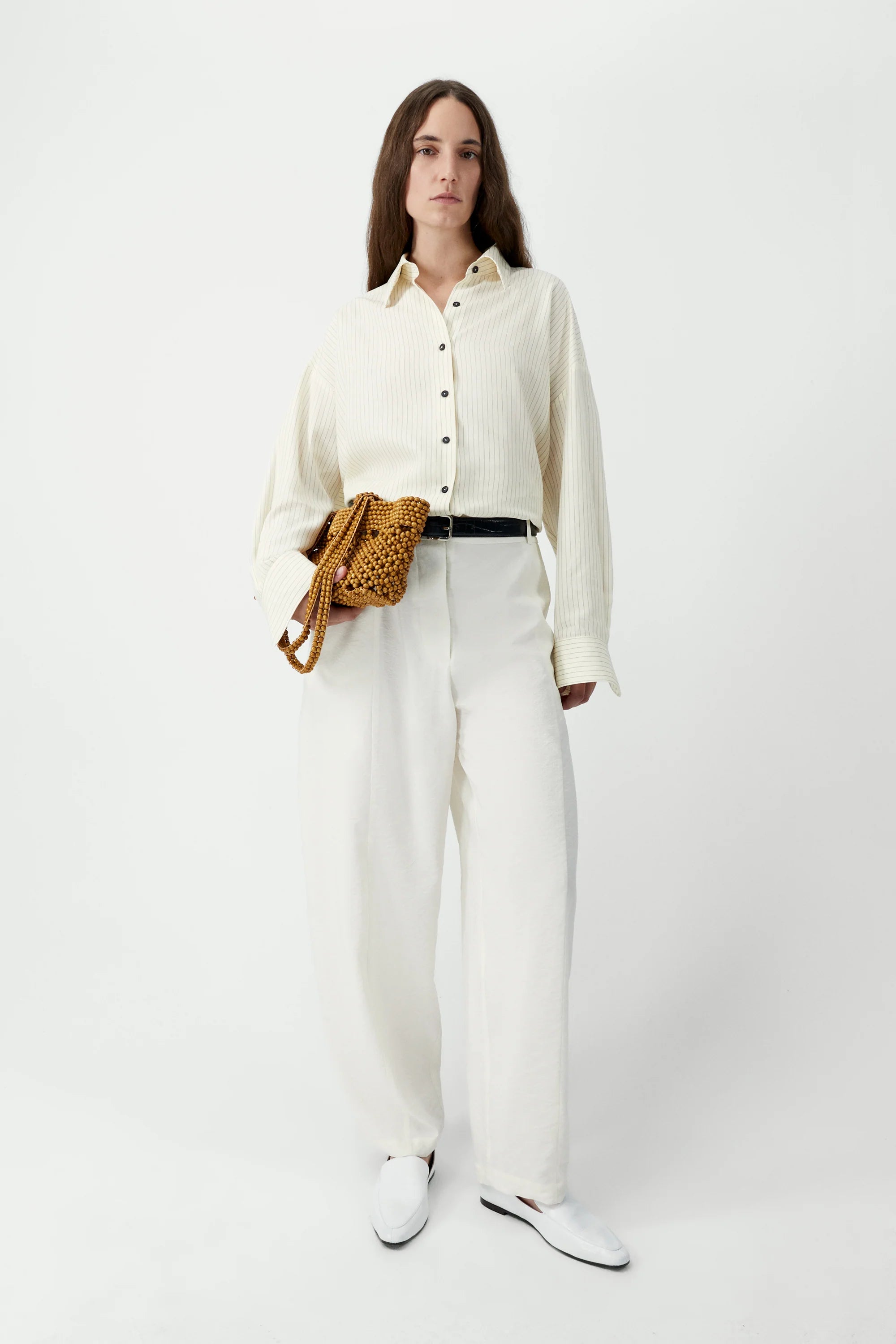 Woman wearing a white outfit with a textured bag on a white background