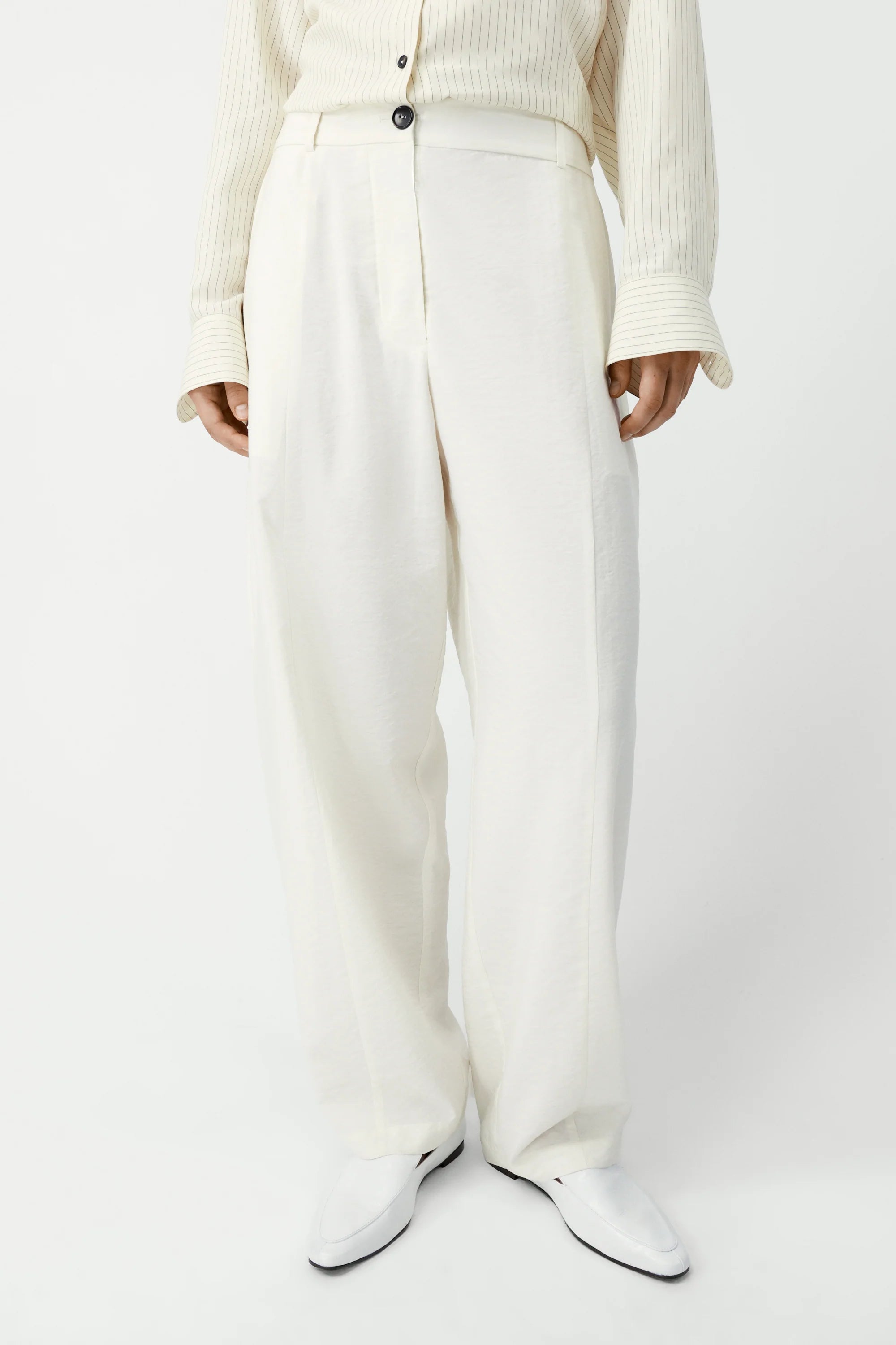 Person wearing white pants and a cream sweater on a plain background