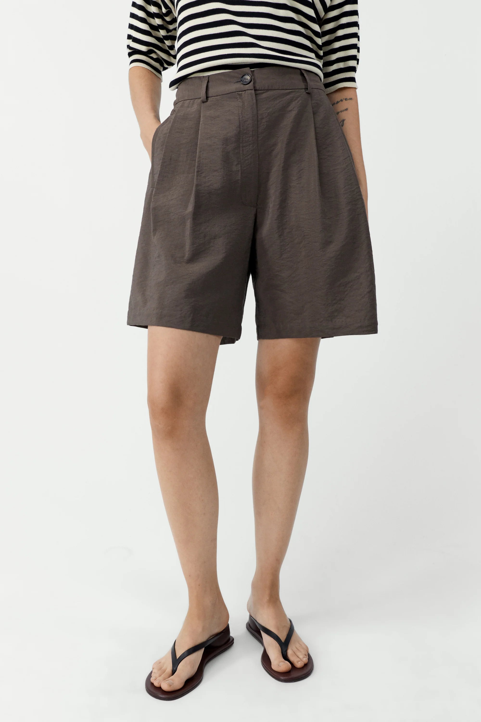 Person wearing brown shorts and a striped shirt on a white background